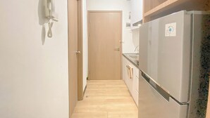 A narrow hallway with a wooden door at the end, a white wall-mounted phone, and a stainless steel refrigerator with a freezer compartment. - Modern Studio Apartment At Cordova Edupartment Semarang (Semarang)