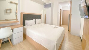 A modern hotel room with a bed, a desk, a chair, a TV, and a wardrobe. - Modern Studio Apartment At Cordova Edupartment Semarang (Semarang)