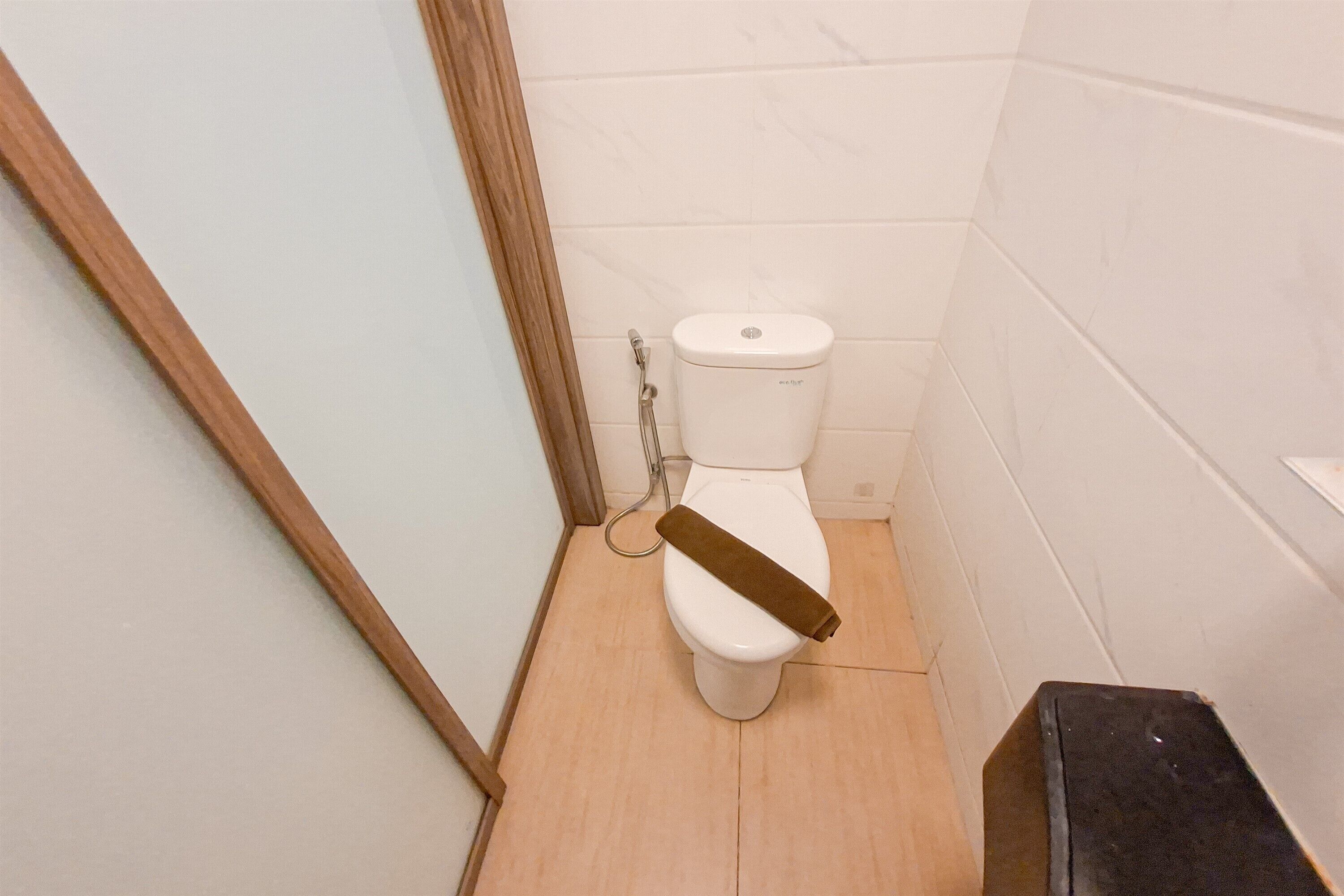 A small, narrow bathroom with a toilet, a shower, and a wooden floor.
