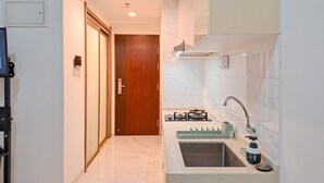 A modern kitchen with a built-in gas stove, a sink, and a wooden door leading to another room. - Simply Look Studio Room At Sky House Bsd Apartment (Pagedangan)