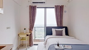 A hotel room with a bed, a desk, and a view through the window. - Simply Look Studio Room At Sky House Bsd Apartment (Pagedangan)