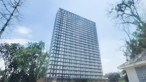 Un edificio moderno e slanciato con facciata in vetro, circondato da piante e un'area pavimentata antistante.
