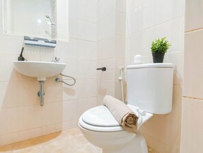 A bathroom with a white sink, toilet, and a small potted plant on the toilet tank. - Cozy Stay Studio Room At Dave Apartment (Depok)
