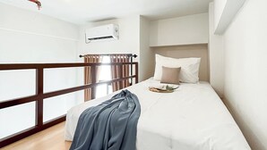 Ein Schlafzimmer mit einem Bett, einem Fenster mit Vorhängen, einer Holzreling und einer Klimaanlage.