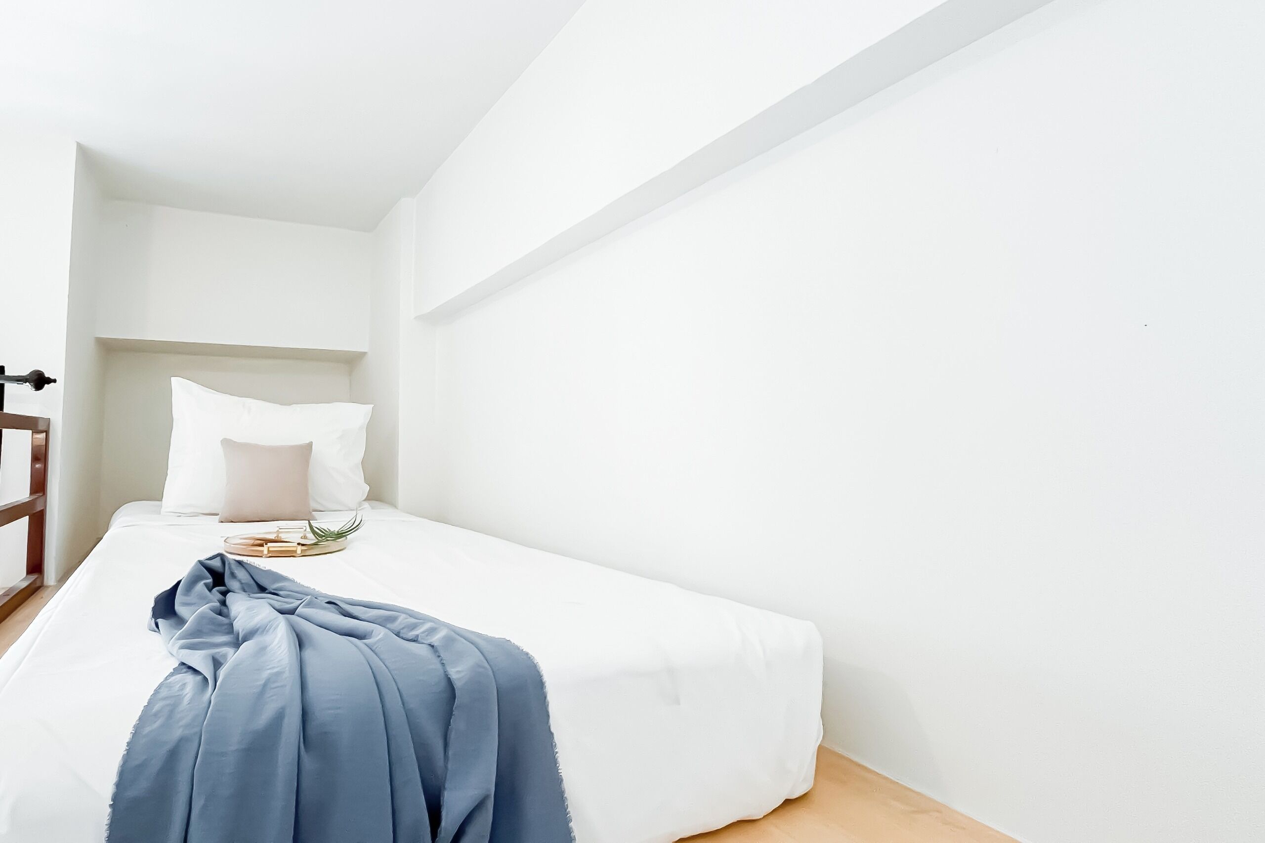 A neatly made bed with white bedding and a blue blanket, a wooden headboard, and a small bedside table with a plant.
