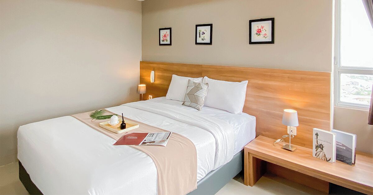 Une chambre d’hôtel avec un lit, des tables de chevet, une petite table et des tableaux encadrés au mur.
