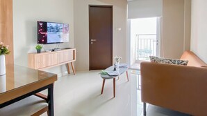 Ein modernes Wohnzimmer mit einem Flachbildfernseher, einer Holzkassette, einem Glastisch, einer Couch und einem Balkon mit Geländer.