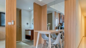 Une pièce moderne avec un séparateur en bois, un bureau blanc avec deux chaises, un miroir et une petite table ronde sur laquelle est posé un vase.