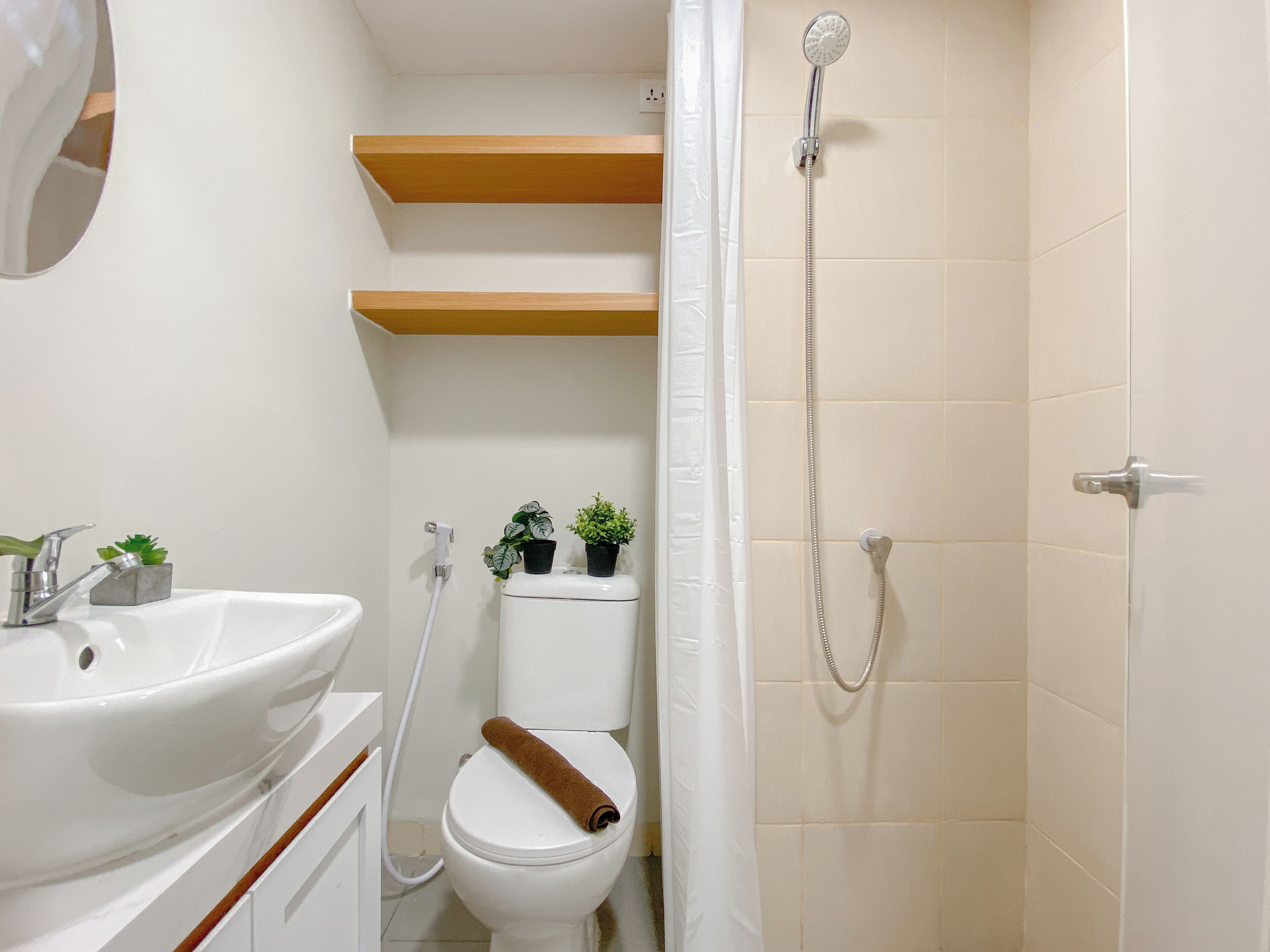 A bathroom with a white sink, toilet, and shower. There are wooden shelves above the toilet and a towel on the toilet seat.
