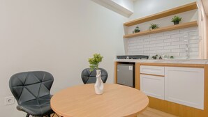 Moderni keittiö, jossa on pyöreä puinen pöytä, kaksi mustaa tuolia, valkoinen maljakko kukkineen, sisäänrakennettu astianpesukone ja valkoinen tiiliseinä takana.