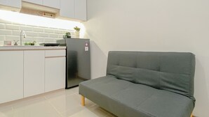 A compact kitchen with white cabinets, a built-in refrigerator, and a grey sofa against the wall. - Best Deal And Homey Studio At Meikarta Apartment (Cikarang)