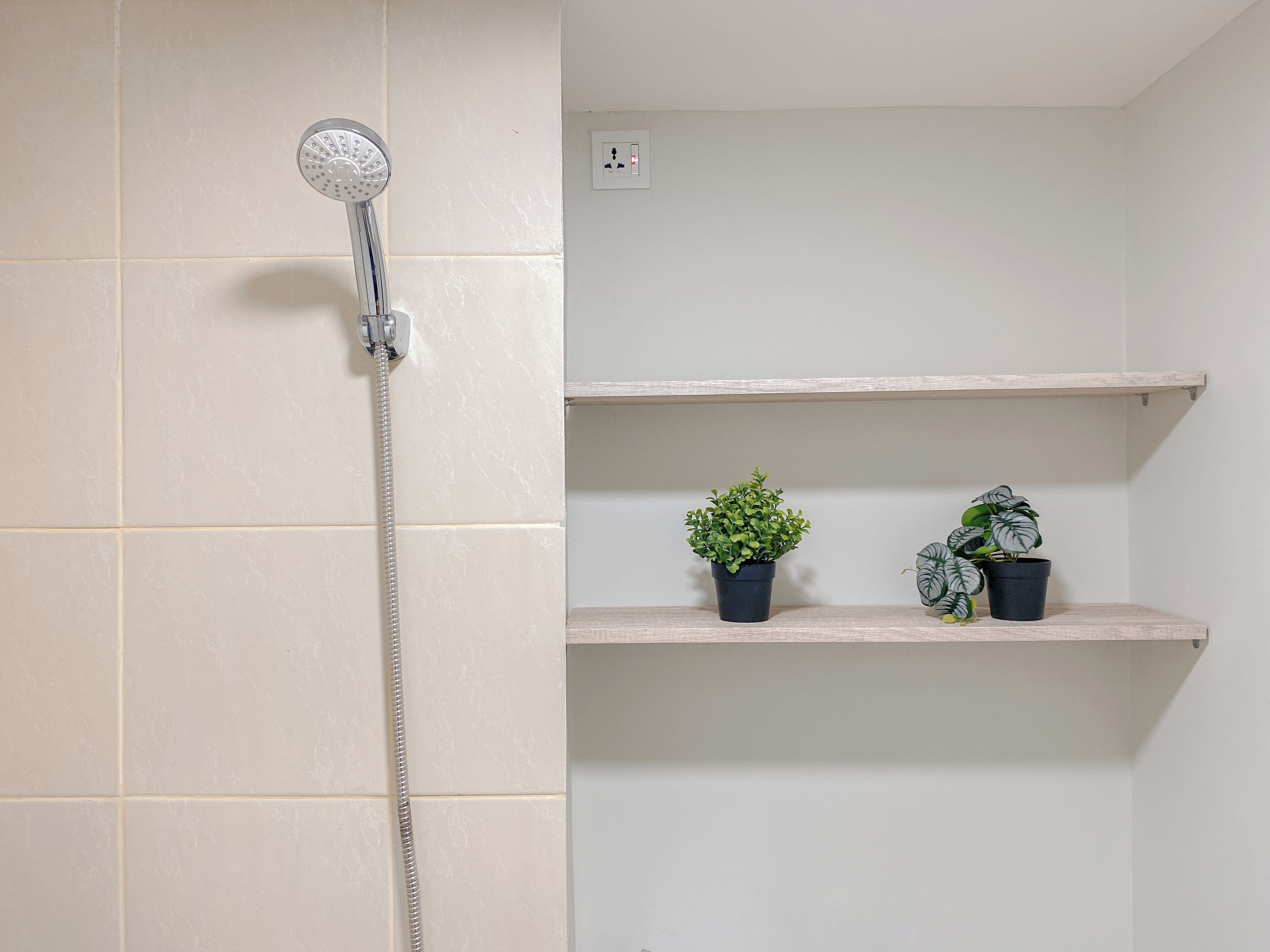 A bathroom with a shower, tiled walls, and two shelves with potted plants.