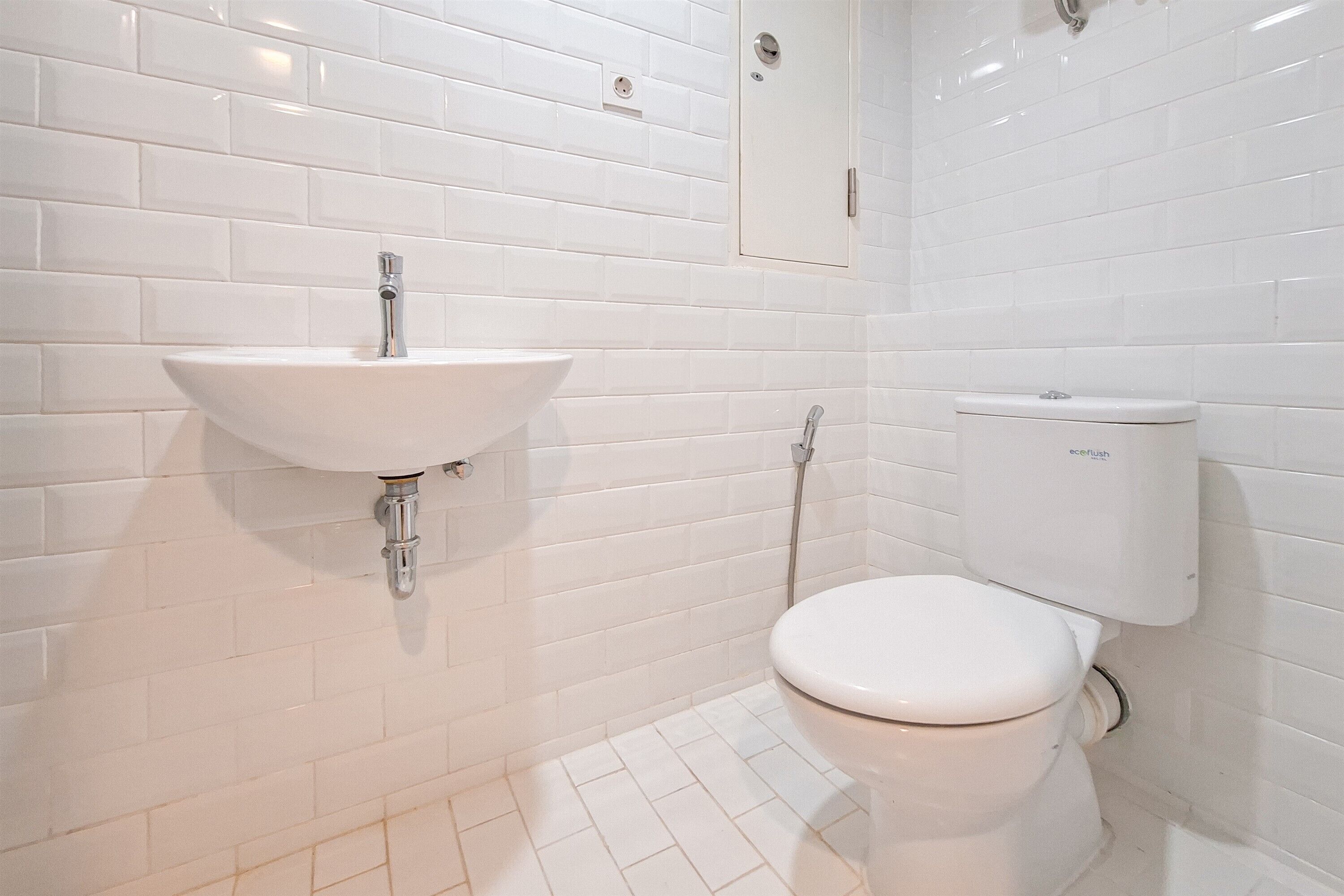 A bathroom with white subway tiles, a white sink with a chrome faucet, and a white toilet with a tank.