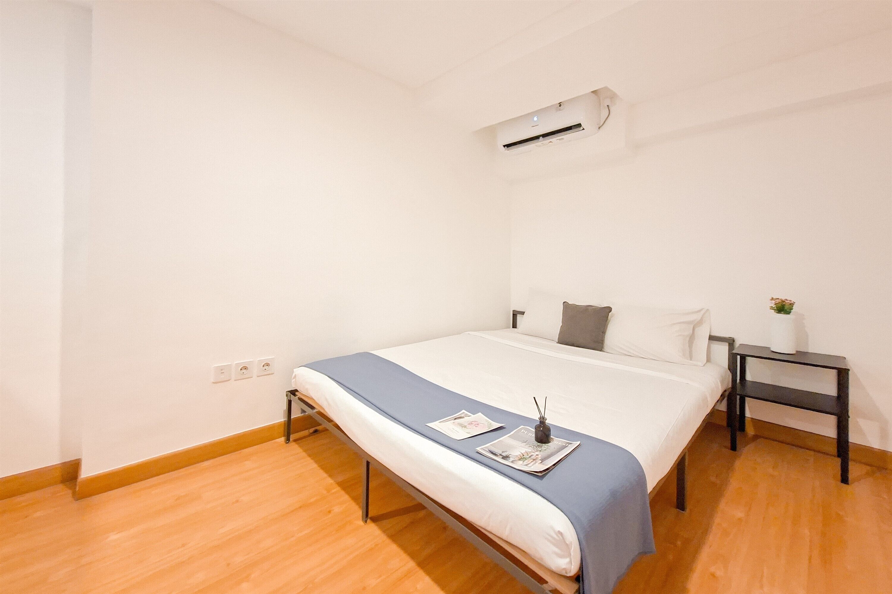 A minimalist bedroom with a single bed, a nightstand, a small table, and a wall-mounted air conditioner.
