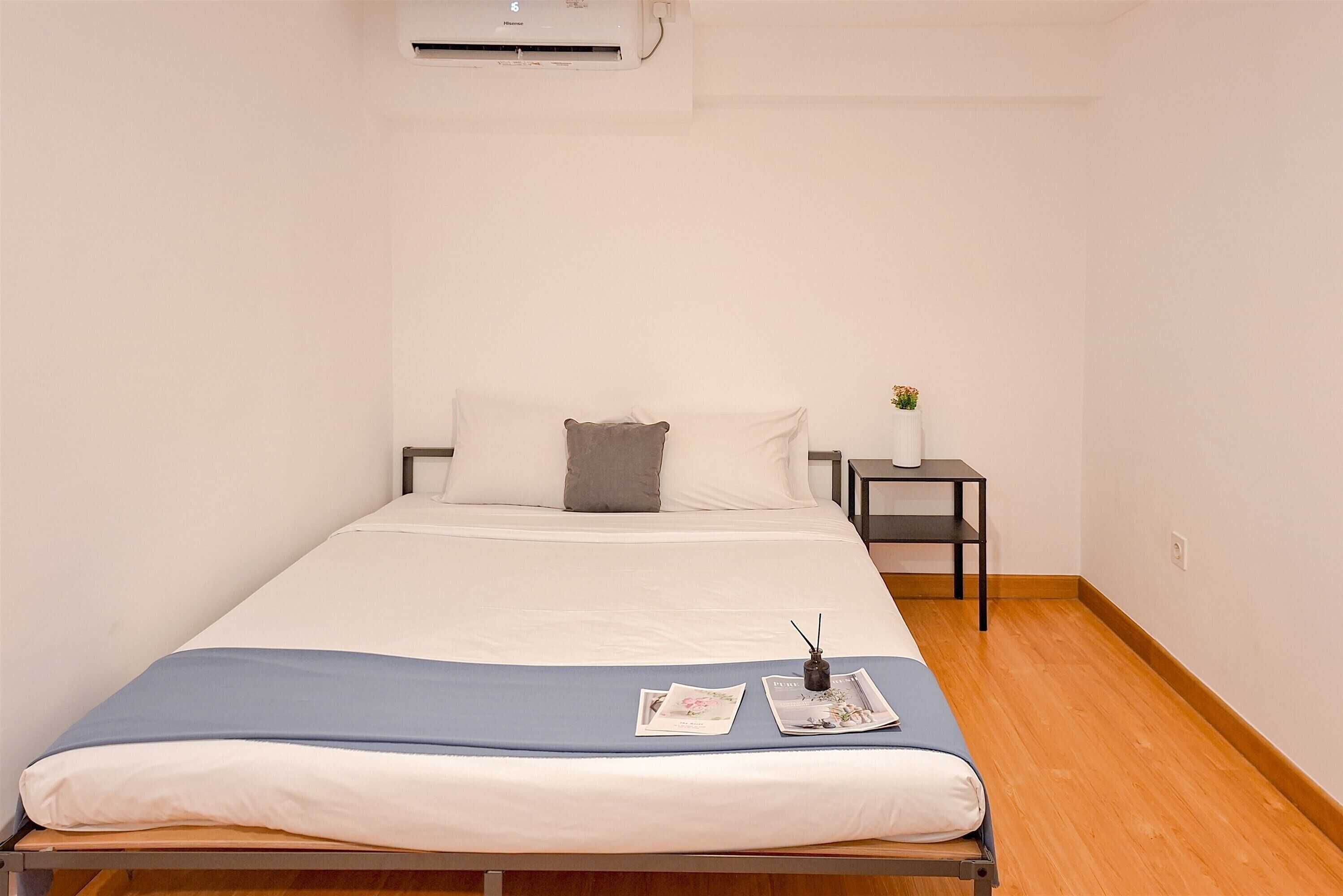 A neatly made bed with a blue blanket, a pillow, and a small bedside table with a vase of flowers.
