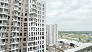 A high-rise residential building with multiple balconies and a view of a green landscape and another building in the distance. - Good And Enjoy Living Studio At Tokyo Riverside Pik 2 Apartment (Teluknaga)
