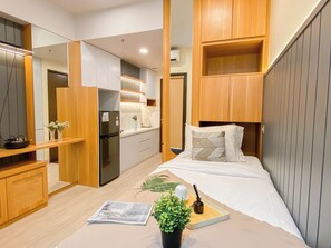 A compact bedroom with a bed, bedside table, and a small kitchenette. - Chic And Cozy Studio At Apartment Transpark Cibubur (Depok)