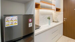 A modern kitchen with a stainless steel refrigerator, white cabinets, a marble backsplash, and a wooden door. - Chic And Cozy Studio At Apartment Transpark Cibubur (Depok)