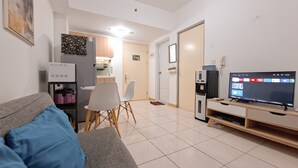 A living room with a grey sofa, a television, and a dining area with a table and chairs. - Nice And Homey 2Br Apartment M-Town Residence (Gading Serpong)