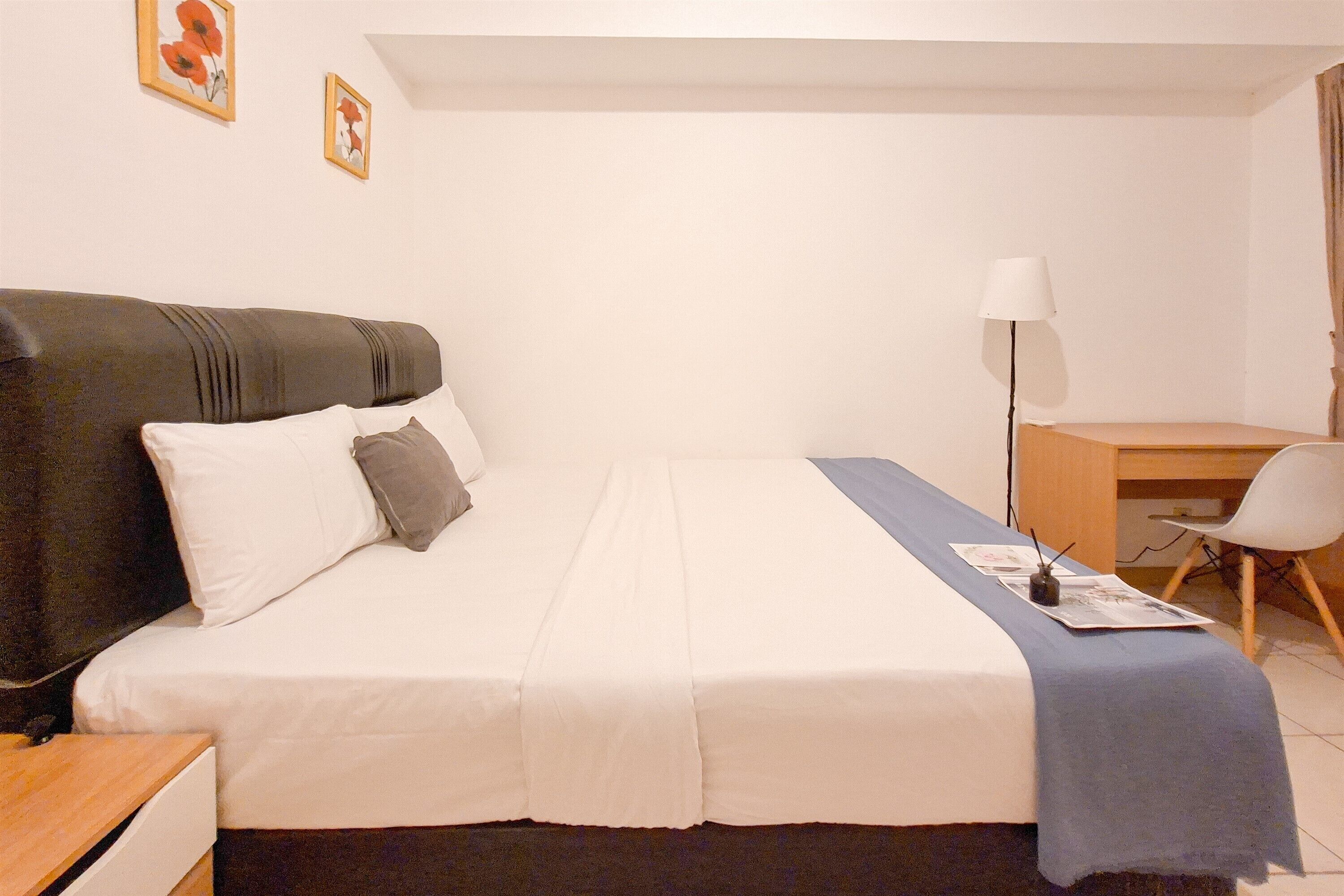A neatly arranged bedroom with a bed, bedside table, lamp, chair, and desk.