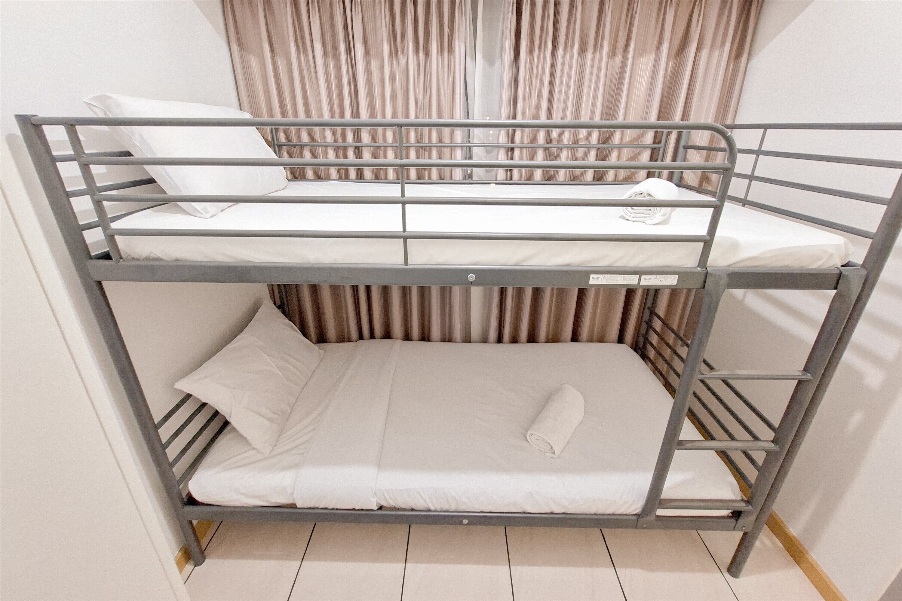 A bunk bed with two levels, white bedding, and a curtain in the background.