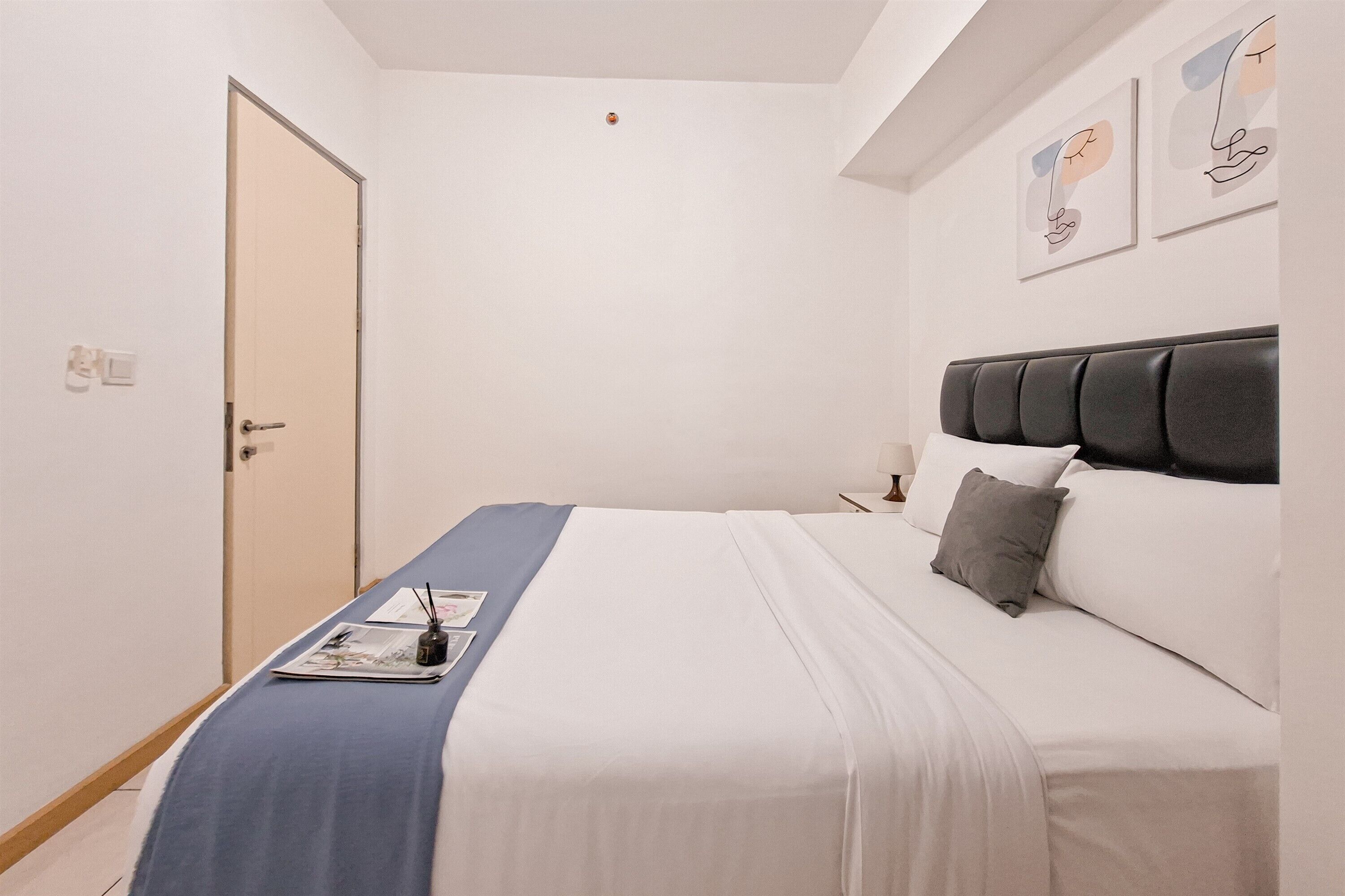 A neatly made bed with a blue and white bedspread, a gray pillow, and a bedside table with a lamp and a small object.