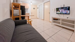 A living room with a grey sofa, a wooden TV stand, a flat-screen TV, and a kitchen area in the background. - Best Location And Homey 2Br Apartment At M-Town Residence (Gading Serpong)
