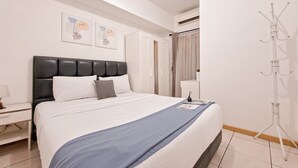 A neatly made bed with a blue blanket, a white bedside table with a lamp, and a coat rack. - Best Location And Homey 2Br Apartment At M-Town Residence (Gading Serpong)