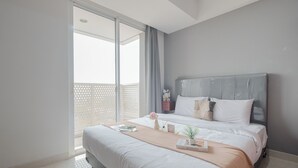A modern hotel room with a large bed, a view of the sky through a balcony, and a neatly made bed with a beige throw blanket and a small plant. - Cozy Stay Studio At West Vista Apartment (Jakarta)