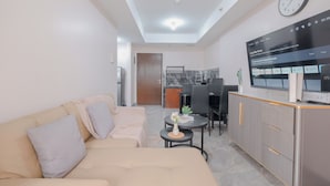 A modern living room with a sofa, a small table with a vase, and a kitchen area with a dining table and chairs. - Prime Location 1Br At The Wave Kuningan Apartment (Jakarta)