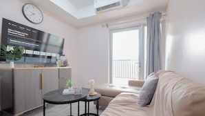 A modern living room with a sofa, a round table, a TV mounted on the wall, and a window with curtains. - Prime Location 1Br At The Wave Kuningan Apartment (Jakarta)