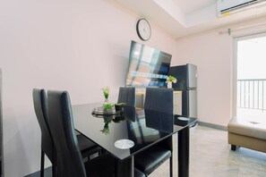 Un espace repas moderne avec une table en verre, des chaises noires, une horloge au mur et un téléviseur à écran plat.