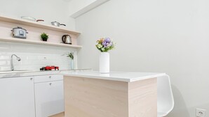 A modern kitchen with white cabinetry, a built-in island, and a small potted plant. - Neat Studio Room Apartment Meikarta (Cikarang)