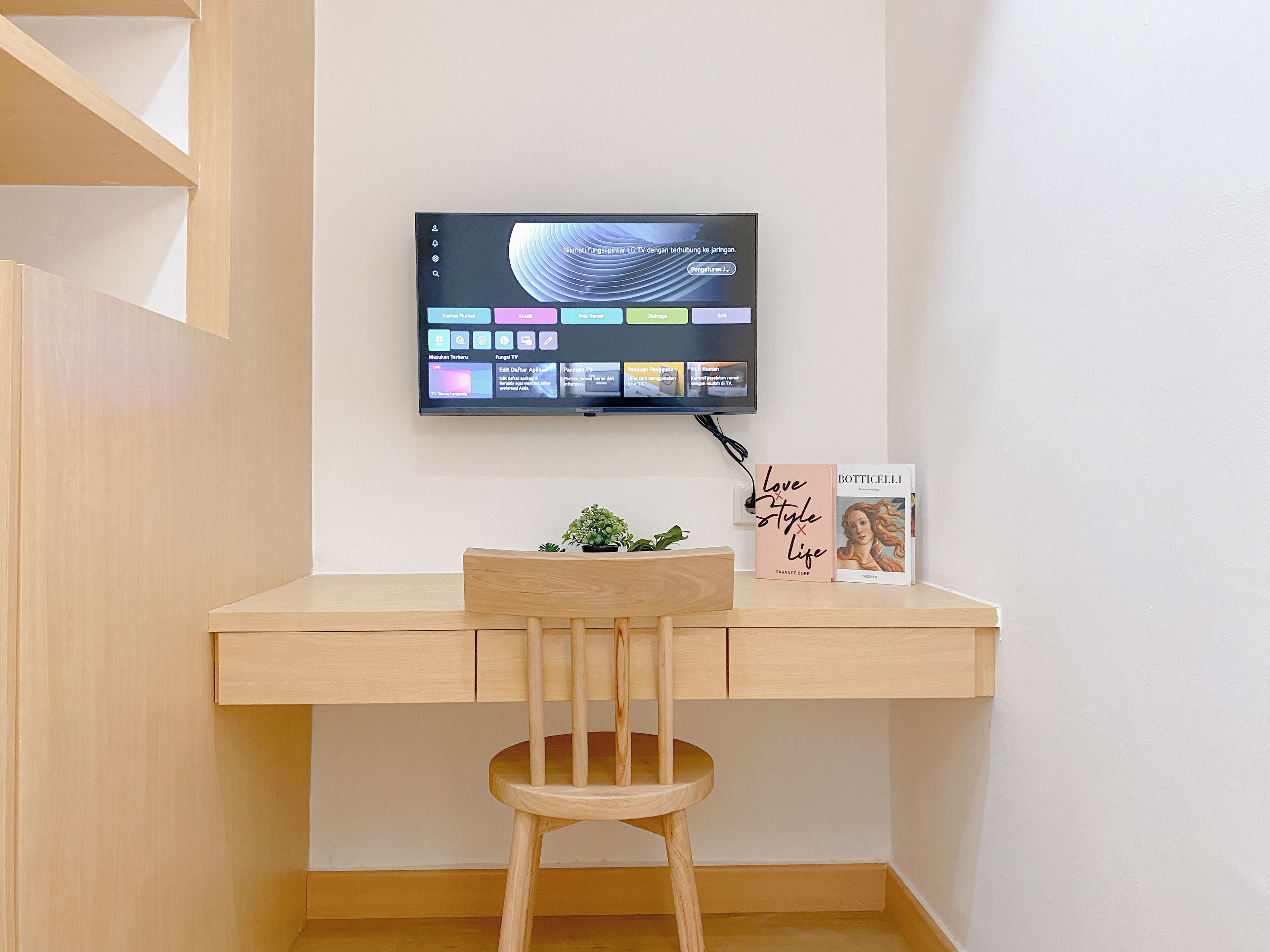 A wooden desk with a mounted TV displaying a colorful interface, a potted plant, and a book titled 'Love Style Life'.