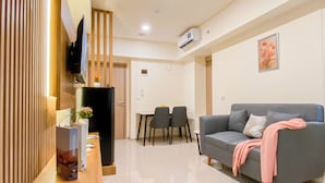 A modern living room with a grey sofa, a wooden sideboard, and a dining area with two chairs and a table. - Comfy Apartment 2Br At Meikarta (Cikarang)