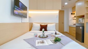Ein modernes Hotelzimmer mit Bett, Fernseher, einer kleinen Küchenzeile und einem Badezimmer.