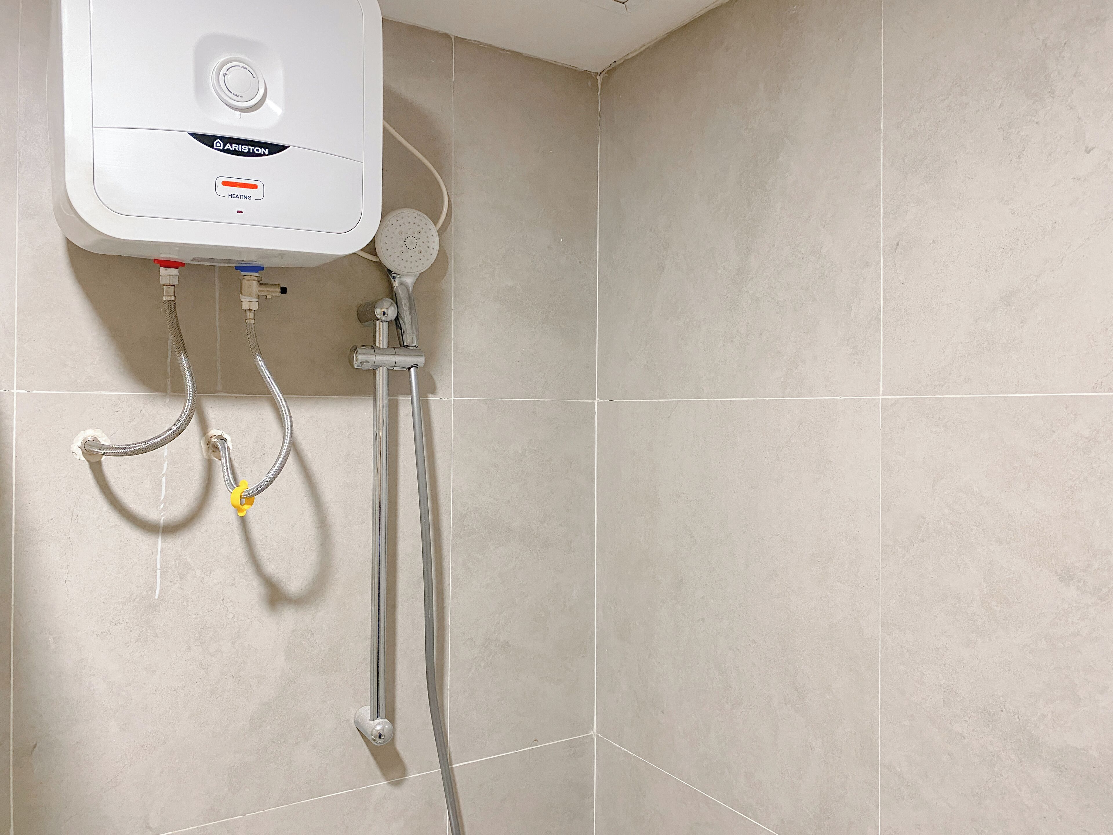 Un baño con calentador de agua blanco, cabezal de ducha y ducha de mano.