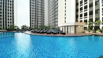 Piscina com espreguiçadeiras e edifícios altos ao fundo.
