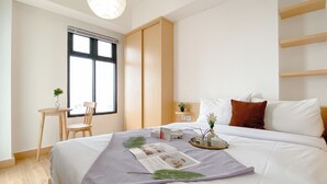 Ett modernt hotellrum med en stor säng, ett skrivbord med en stol, ett fönster med persienner och en liten växt på skrivbordet.