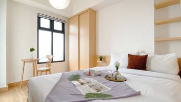 Quarto de hotel moderno com uma cama grande, uma mesa com cadeira, uma janela com persianas e uma pequena planta na mesa.