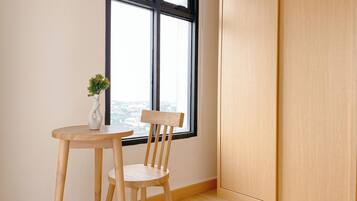 Quarto com uma mesa e cadeira de madeira, um vaso branco com planta e uma janela com vista para a cidade.