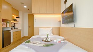A hotel room with a bed, a small kitchenette, a flat-screen TV, and a wooden ceiling. - Restful And Tidy Studio At Pollux Chadstone Apartment (Cikarang)