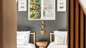 Ein Schlafzimmer mit zwei Betten, einem Fenster mit Blick auf Grünflächen, einem Deckenventilator und gerahmten Bildern an der Wand.