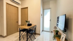 Una habitación pequeña y limpia con un escritorio de madera, dos sillas, un televisor y una puerta que da a otra habitación.