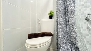 A bathroom with a toilet, a small potted plant, and a patterned shower curtain.