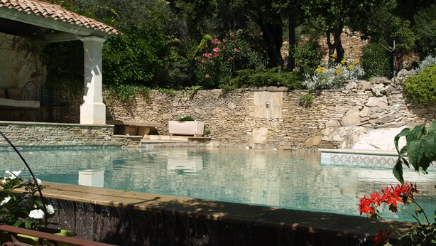 Un área de piscina con un muro de piedra, una pérgola y un edificio de piedra.