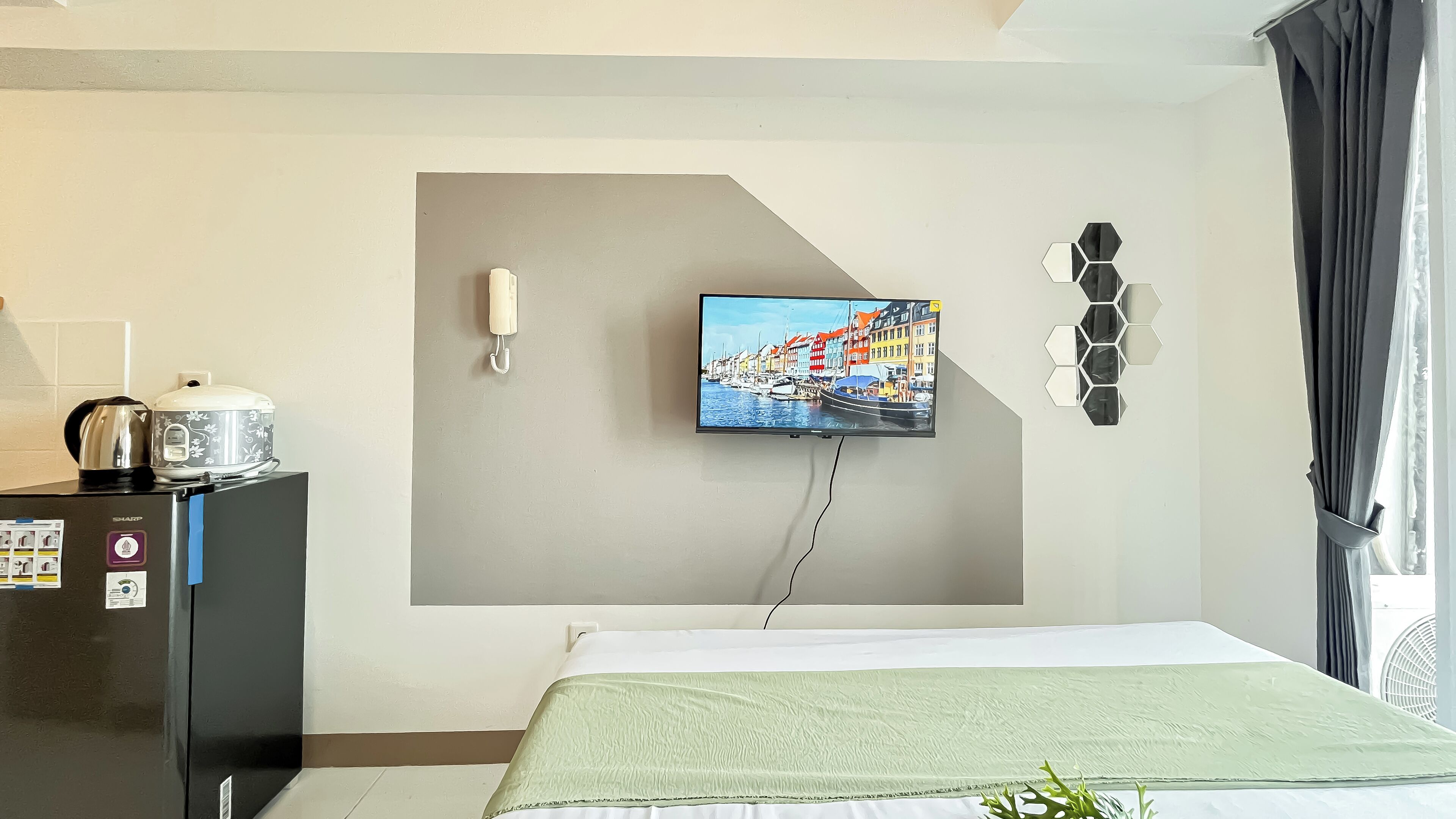 Una camera d'albergo con un letto, una TV a parete, un bollitore, una macchina per il caffè e un tavolino con una pianta.