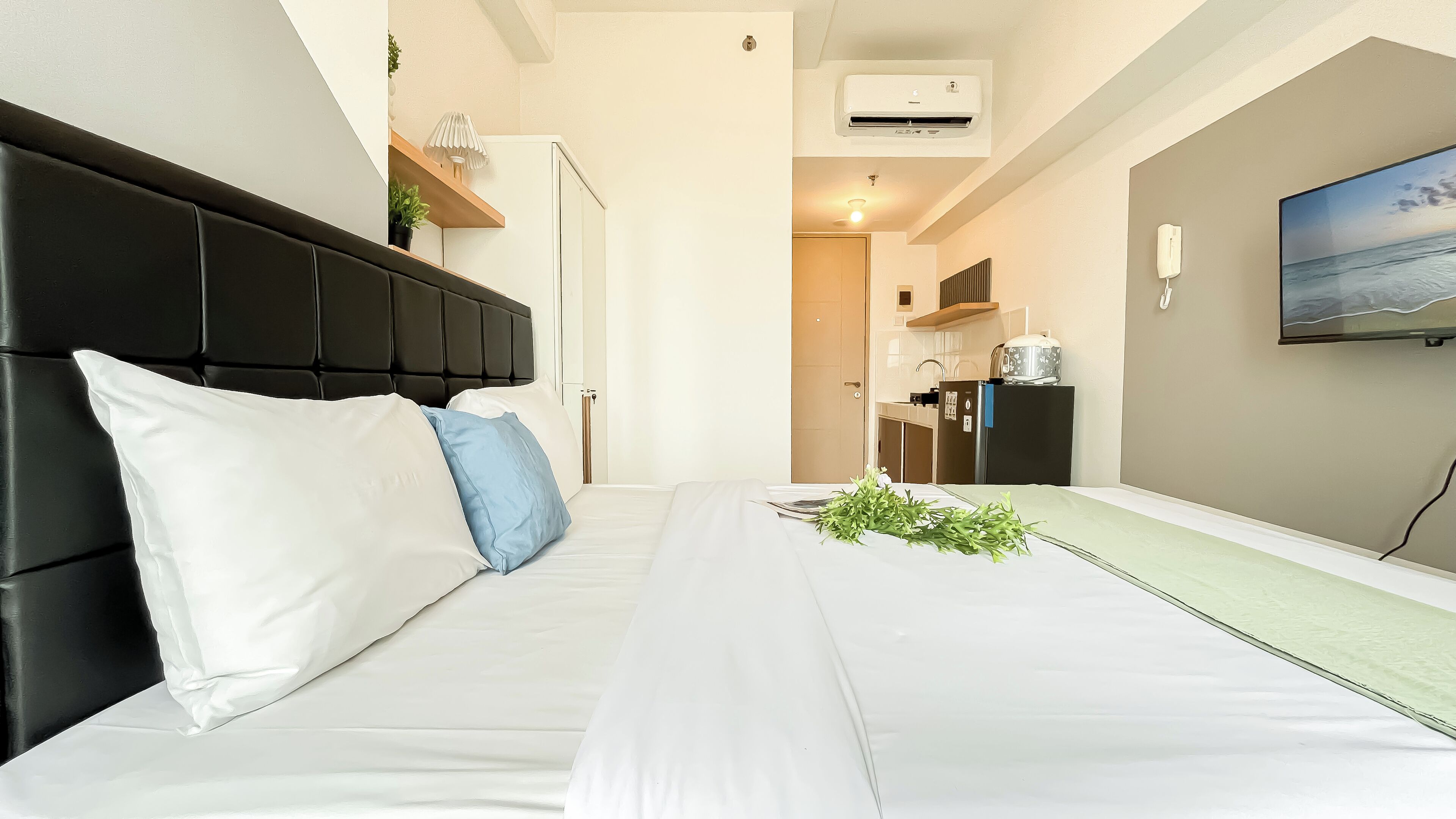 Een hotelkamer met een bed, een televisie aan de muur en een kitchenette op de achtergrond.