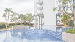 Una piscina con bordi piastrellati, circondata da palme e un edificio a più piani con balconi.