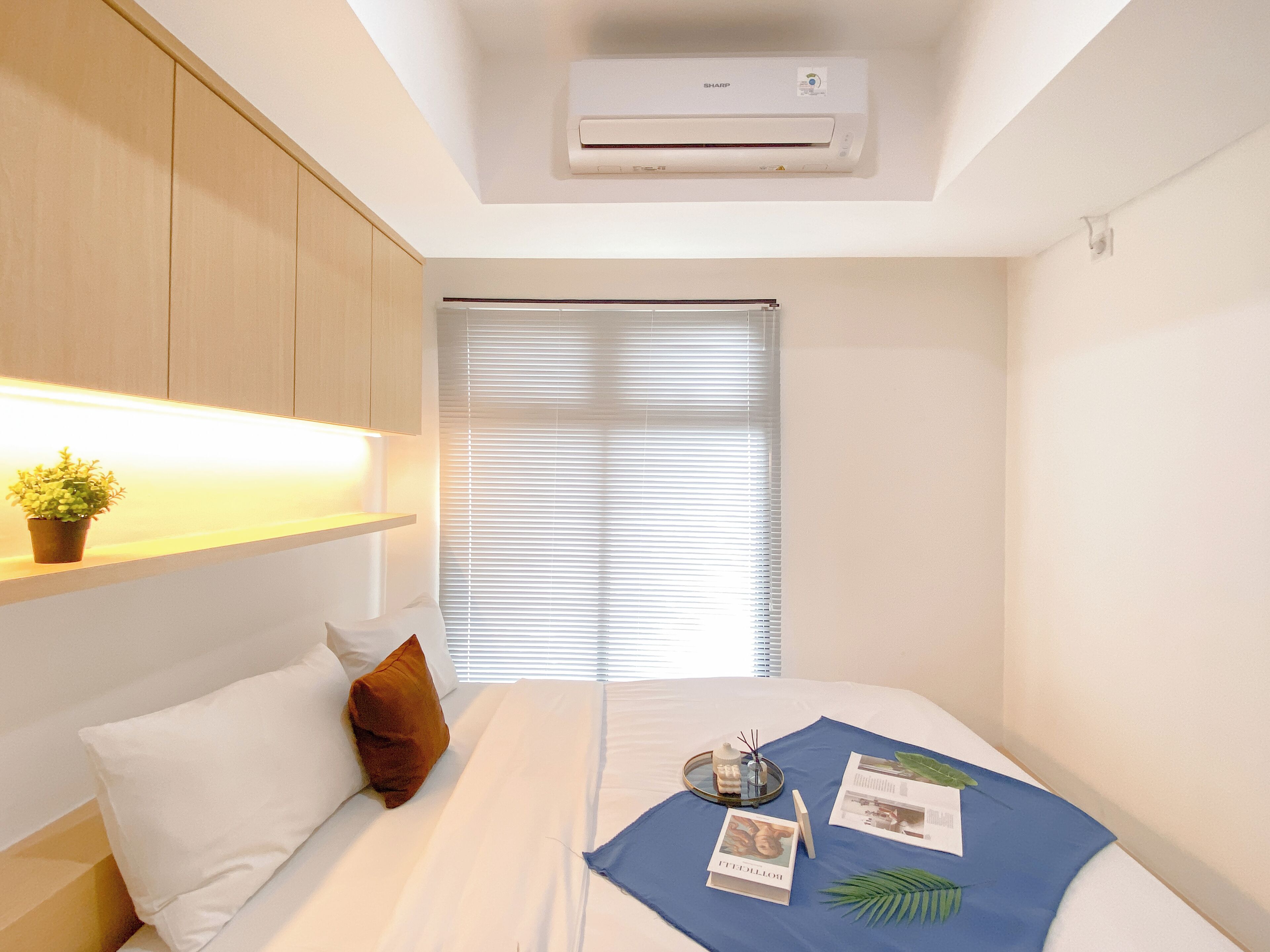 Ein Hotelzimmer mit einem Bett, einem Nachttisch mit Pflanze, einem Fenster mit Jalousien und einer Klimaanlage an der Decke.